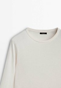 Pull blanc à manches longues avec col rond côtelé et étiquette noire cousue à l'intérieur de l'encolure sur fond blanc uni.