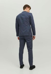 Tmavomodrý oblek na mieru s textúrovaným povrchom. Slim-fit dizajn so zúženými klopami a zodpovedajúcimi nohavicami. Čierne topánky dotvárajú vzhľad.