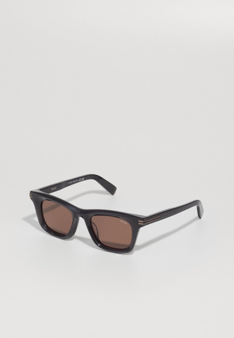 Black rectangular sunglasses with brown lenses, featuring thin gold accents on the temples and textured arms. Lightweight plastic frame.