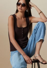 Maiou maro închis cu dungi, decolteu pătrat și detaliu cu nasturi, asortat cu blugi largi, colorați în albastru deschis, și sandale argintii. Model purtând ochelari de soare.