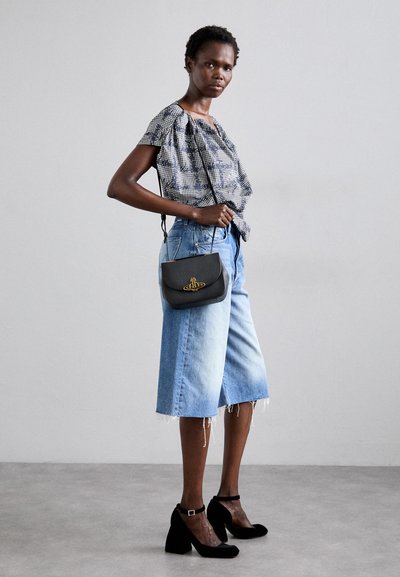 Bluză cu imprimeu alb-negru, culottes din denim cropped cu margine desfăcută, geantă neagră cu accesorii aurii și pantofi cu toc negri.
