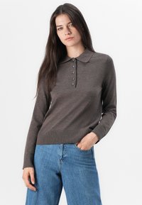 Polo shirt marron à manches longues avec un col, patte de boutonnage à cinq boutons et ourlet côtelé, associé à un jean taille haute bleu clair.