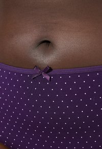 Paarse onderbroek met stippen en een gladde textuur, voorzien van een klein satijnen strikje op de tailleband.