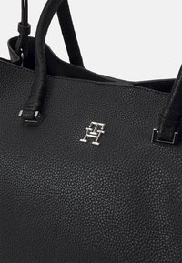 Bolso tote de cuero negro con superficie texturizada. Presenta un diseño estructurado, acento de logo plateado y dos asas.