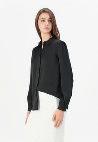 Black silk blouse with a collared neck, button-down front, and long sleeves. Smooth texture and slightly loose fit.