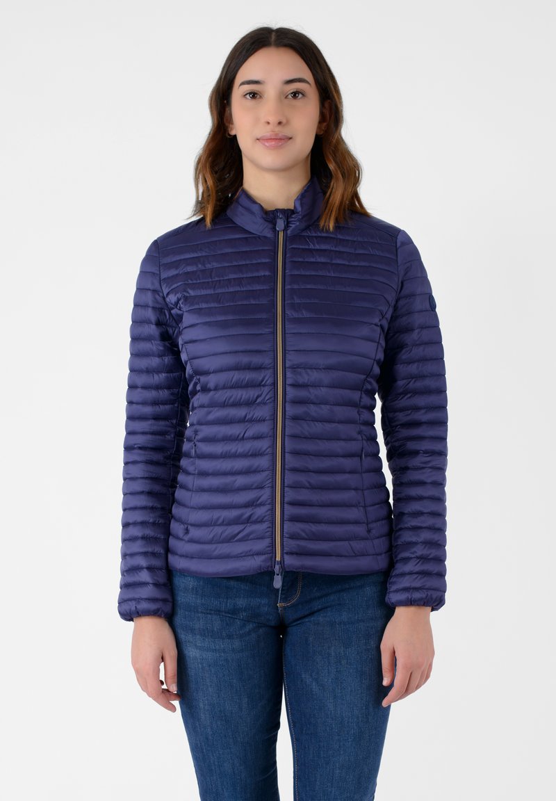 Giacca imbottita blu navy con zip frontale, texture a coste e colletto alto. Presenta un design aderente con polsini elasticizzati.