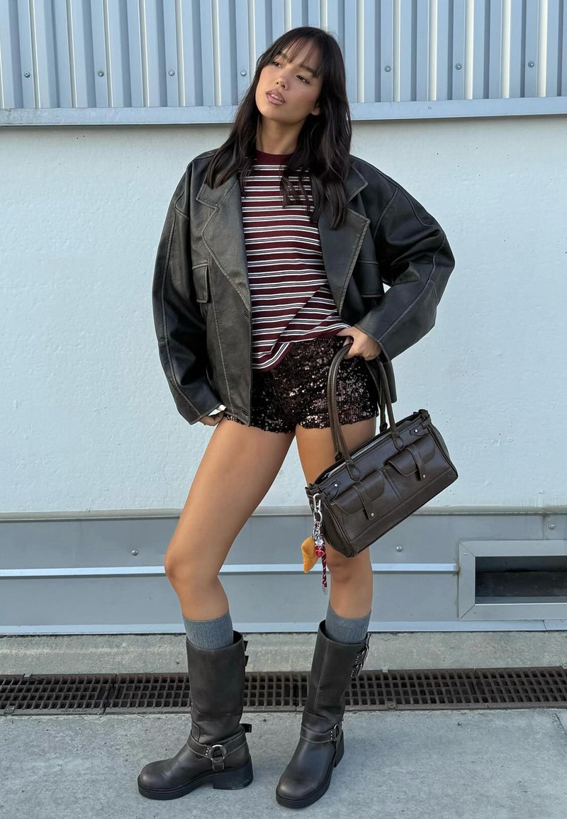 Svart läder oversized jacka, bordeaux- och vitrandig skjorta, paljettprydda svarta shorts, knähöga grå strumpor, svarta ankelskor, liten mörk handväska.