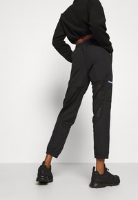 Joggers negros ajustados con puños elásticos, que presentan paneles de malla y un acento azul en contraste. Combinados con zapatillas deportivas negras.