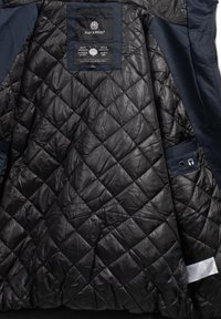 Schwarze gesteppte Jackeninnenseite mit satinierter Oberfläche, mit einem Etikett und einem Kopfhöreranschluss aus blauem Stoff auf der linken Seite.