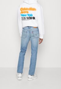 White cropped hoodie with multicolor text on back, paired with light blue straight-leg jeans featuring two back pockets and a brown patch.