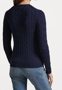 Marinblå kabelstickad tröja med långa ärmar, ribbad halsringning och fåll. Mjuk textur med ett tjockt mönster, tillsammans med ljusblå denimjeans.