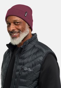 Berretto di maglia bordeaux e gilet imbottito nero con un motivo a diamante; il gilet presenta un'etichetta con il logo sul petto e una zip frontale.