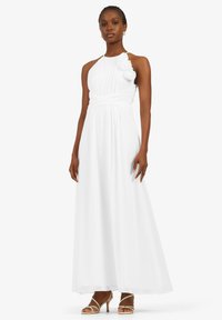 Weißes Halterkleid mit gepufftem Oberkörper und floralen Akzenten. A-linien Silhouette, knöchellang, aus leichtem Stoff. Beigefarbene Riemchensandalen.