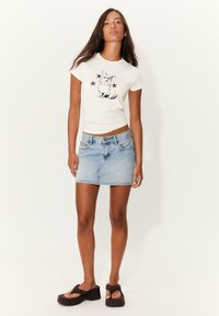 Hvid tætsiddende t-shirt med kanin- og stjernesgrafik; blå denim miniskirt; brune platformsandaler. Simpelt, afslappet sæt.