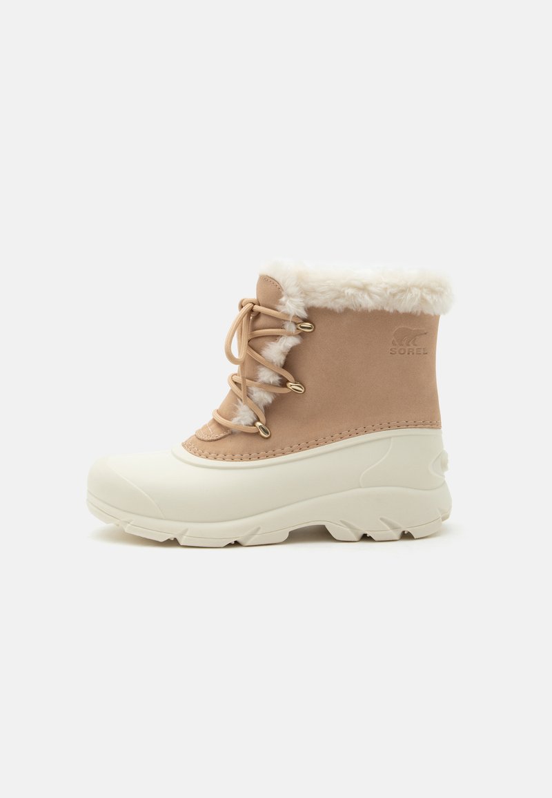Botte d’hiver mi-hauteur avec dessus en daim beige, semelle en caoutchouc blanche, bordure en fausse fourrure et lacets à l’avant.