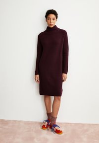 Robe tricotée en côtes de couleur bourgogne profond avec un col montant. Associée à des baskets colorées et des chaussettes texturées. Design simple et ajusté.