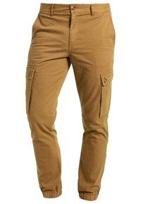 Beige cargobyxor i bomull med elastiska muddar, flera sidofickor och knappstängning i midjan. Slät textur.