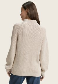Pull en maille côtelée beige clair avec un col montant, des épaules abaissées et une coupe décontractée, doté de manches larges et d'un tissu texturé.