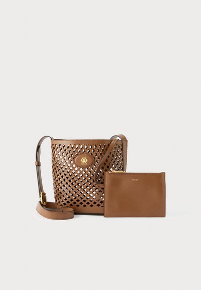 Καφέ δερμάτινη τσάντα ώμου με μοτίβα πλέγματος, ρυθμιζόμενο λουρί, χρυσή πλακέτα με λογότυπο και συνοδευτικό απλό τσαντάκι με φερμουάρ δίπλα της.