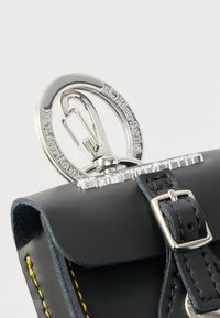 Μαύρη δερμάτινη τσάντα με ασημένια εξαρτήματα, που διαθέτει κυκλικό κούμπωμα, χαραγμένες λεπτομέρειες και κίτρινες ραφές στα άκρα.