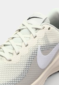 Lichtgrijze Nike hardloopschoen met een mesh-textuur, witte accenten en een prominente swoosh-logo aan de zijkant. Gelaagde ontwerp met een lichtkleurige veters.