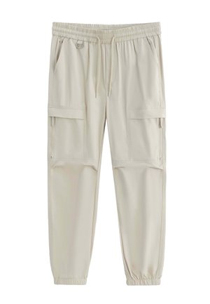 Pantalons cargo beige clair avec taille élastique et bas de jambes élastiques, cordon de serrage, poches latérales et poches à rabat zippées sur les cuisses.