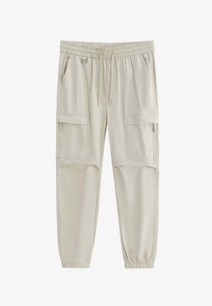 Pantalons cargo beige clair avec taille élastique et bas de jambes élastiques, cordon de serrage, poches latérales et poches à rabat zippées sur les cuisses.