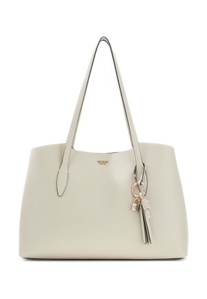Sac cabas en cuir crème avec deux poignées et un pompon décoratif et des breloques accrochés sur le côté droit.