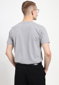 Gray short-sleeve t-shirt in cotton material, featuring a classic crew neckline and a relaxed fit, worn with black pants and a belt.