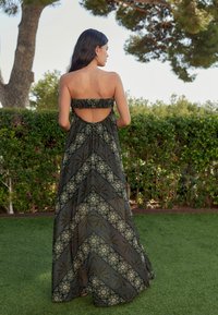 Robe maxi sans bretelles avec un haut volant, présentant un dos découpé, une silhouette fluide et des motifs floraux délicats en vert et or.