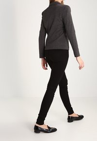 Zwarte fitted broek met een gladde textuur, gecombineerd met een grijze blazer, gezien vanuit de achterkant, die een strakke en op maat gemaakte uitstraling toont.