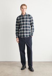 Kockás gombos ing sötétkék és zöld színben, széles gallérral és felhajtott ujjal. Sötét nadrággal és fekete cipővel viselve. Sima textúrájú.