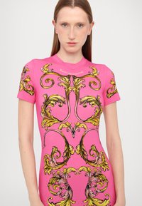 Top aderente a maniche corte di un vivace colore rosa con motivi floreali barocchi in oro e nero. Tessuto liscio con scollo a girocollo.