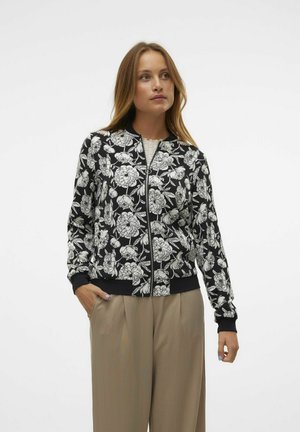 Giacca bomber floreale con uno sfondo nero e fiori bianchi, polsini e orlo a coste, e chiusura frontale con zip.