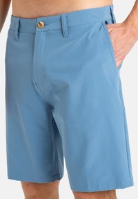 Pantalones cortos de color azul claro, hechos de una tela suave, con cierre de botón, bolsillos laterales y un corte relajado. Bajo a medida y detalles de costura mínimos.