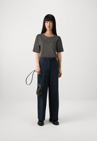 Īsām piedurknēm pelēks tops ar rotājumiem, apvienots ar augsto jostas vietu, tumši zilām platām biksēm un mazu melnu rokassomu.