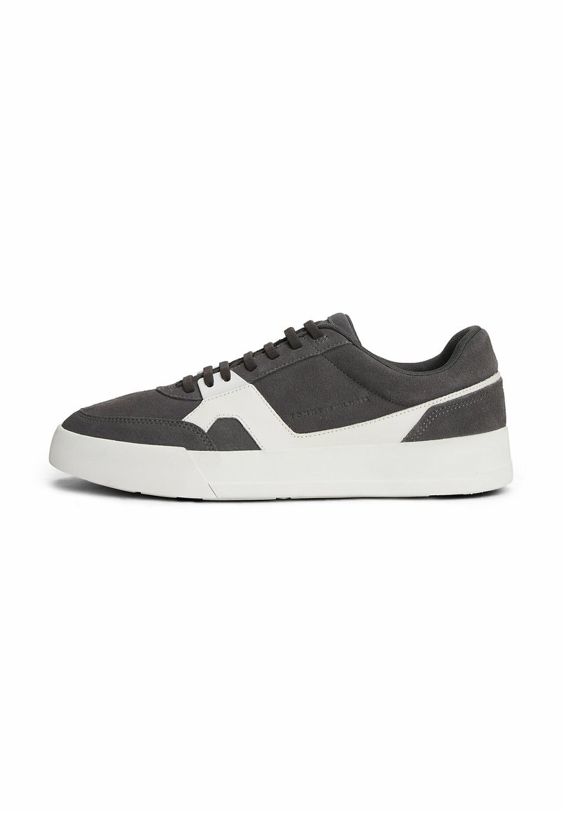 Sneaker in suede grigio con suola in gomma bianca, caratterizzato da un design moderno, lacci piatti e un pannello decorativo sul lato.