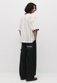 Kurzarm-Polohemd in Cremefarbe mit roten Streifen und einem gerippten Kragen, kombiniert mit lockeren, schwarzen Jeans mit grafischen Akzenten.