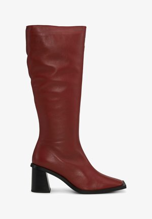 Czerwony skórzany kozak sięgający do kolan z kwadratowym noskiem i grubym czarnym obcasem, charakteryzujący się gładką fakturą i delikatnymi fałdami na cholewce.