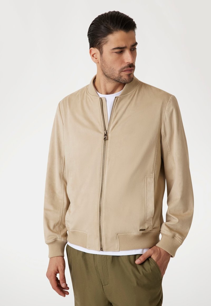 Beige bomberjack gemaakt van gladde stof, met een ritssluiting aan de voorkant, ribbelmanchetten en zijzakken, gedragen over een wit shirt.