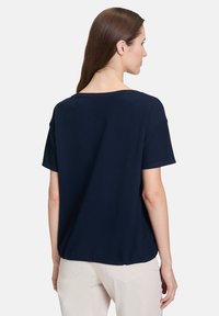 Granatowa bluzka z krótkim rękawem o teksturowanym splocie, okrągłym dekolcie i luźnym kroju, z lekko zaokrąglonym dołem.