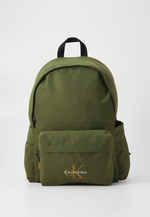 Sac à dos vert olive de forme arrondie, avec une poche zippée à l'avant et un logo Calvin Klein brodé en doré. Fabriqué en tissu durable.