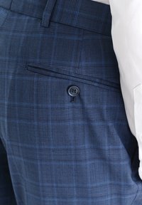 Granatowe spodnie w kratę mają teksturowany materiał, tylną kieszeń z zapięciem na guzik oraz dopasowaną talię.