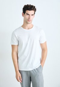 T-shirt blanc à col rond en coton doux et lisse, associé à un pantalon de survêtement gris. Coupe simple et décontractée avec des manches courtes.
