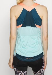 Jasnoniebieski sportowy top na ramiączkach z siateczkowymi akcentami, turkusowymi elementami i koralowymi ramiączkami. Posiada marszczoną talię oraz wyraźne logo na dolnym końcu.