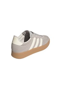 Grauer Adidas Sneaker aus Wildleder mit weißen Streifen, offwhitefarbener Fersenlasche, brauner Gummisohle und Schnürverschluss, Ansicht von hinten rechts.