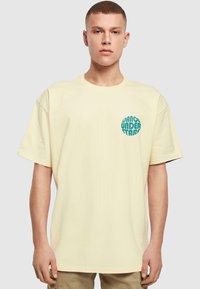 Camiseta de algodón crema con mangas cortas, que presenta un gráfico circular en color azul verdoso que dice "DANCE UNDER STARS" en la parte izquierda del pecho.