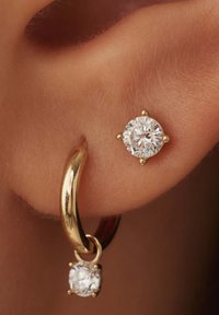 Boucles d'oreilles en or en forme de créole avec une pendaison amovible, dotées d'une pierre en zircon cubique ronde et transparente en monture griffée. Texture lisse, finition polie.