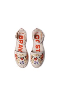 Beige canvas espadrilles with floral embroidery in red, yellow, and purple. Adjustable ankle strap and contrasting orange lettering on the insoles.