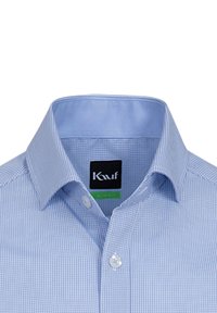 Camicia a quadri blu con colletto azzurro a contrasto, bottoni azzurri e un'etichetta nera con il nome del marchio e un'etichetta verde.